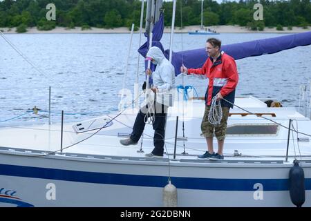 Yachtsmen stand on a deck of sailing yacht with ropes in hands ready to moor to a berth. Amateur regatta devoted to the Day of city. May 30, 2021. Kyi Stock Photo