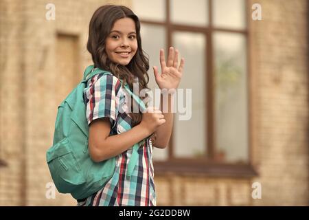 Cute happy girl with long hair in casual style carry travel bag waving goodbye hand gesture outdoors, wanderlust, copy space Stock Photo