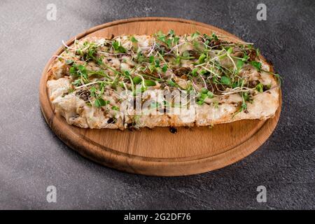 Italian pinsa romana with french escargot grape snails on dark background. Pinsa with snail, cheese, microgreen. Italian gourmet cuisine. Stock Photo