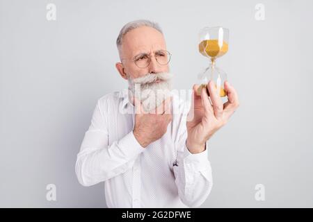 Photo of elderly man pensioner serious think thoughtful look sand timer isolated over grey color background Stock Photo