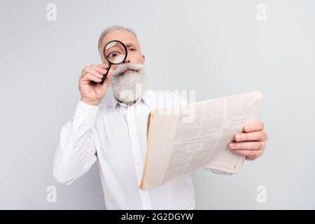 Photo of curious interested old man look magnifier eye newspaper article isolated on grey color background Stock Photo