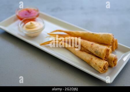 a plate of delicious prawn spring rolls served with dipping sauces on a bar along the Mediterranean coastline Stock Photo