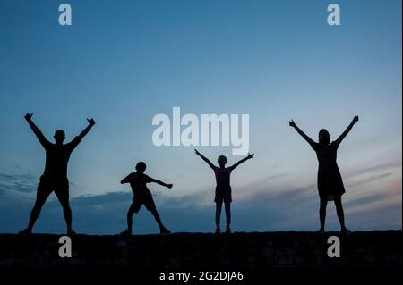 A family of four make shapes and silhouettes against a blue sky Stock Photo