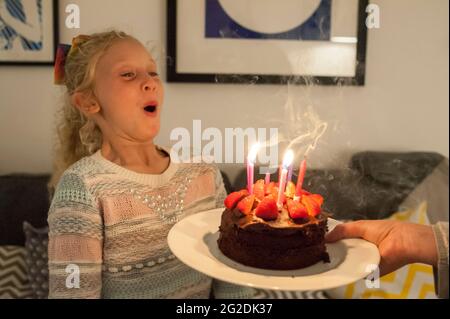 A mother holds out a birthday cake for a little girl on her 7th birthday Stock Photo