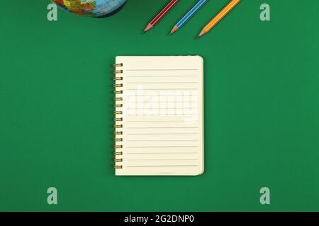 Green school table with blank lined notebook and pencils top view photo with copy space Stock Photo