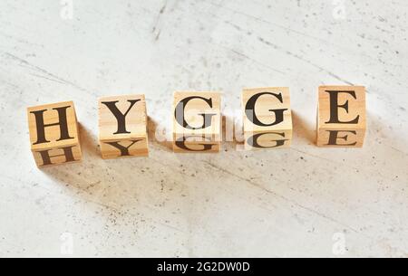 Five wooden cubes with letters HYGGE (scandinavian for word for mood of coziness) on white stone like board, view from above Stock Photo