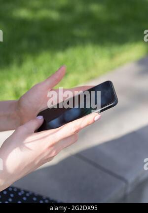 Womens hands with a smartphone in their hands on the background of a green lawn Stock Photo