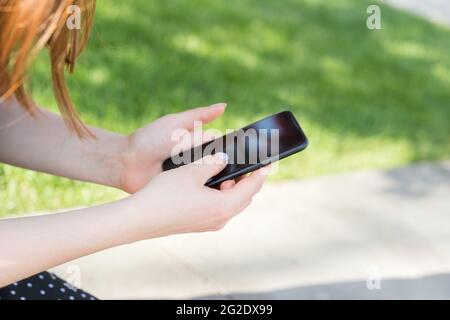 Womens hands with a manicure with a smartphone in their hands on the background of a green lawn Stock Photo