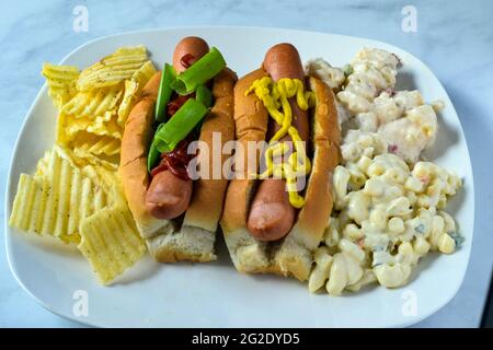 two hot dogs with macaroni and potato salad with chips on the side Stock Photo