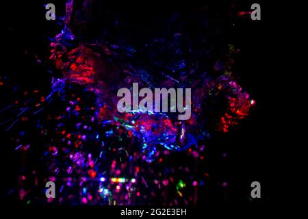 Colored water texture. Splashes of water lit in different colors. Close-up shot of water from the fountain. Bright colors water flow background. Stock Photo