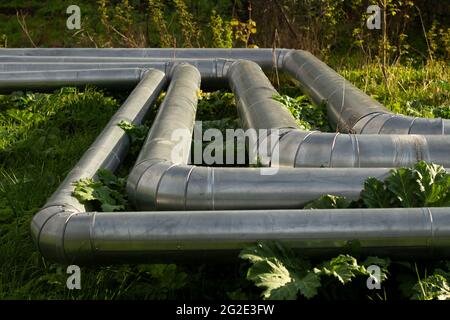Heating pipes on the street. Heat communications in the city. Stainless steel coated industrial pipes. Stock Photo