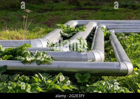 Heating pipes on the street. Heat communications in the city. Stainless steel coated industrial pipes. Stock Photo