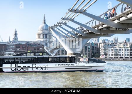 An Uber Thames Clipper River Bus passing under the Millennium Footbridge on the River Thames, London UK Stock Photo