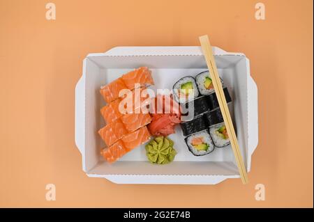 Sushi sets with red ginger and wasabi in a takeaway box. Isolated orange background. Top view. Stock Photo
