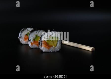 Close-up of a three pieces arranged diagonally of sushi with chopsticks on an isolated orange background.