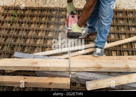Close up on hands of unknown man holding chainsaw at warehouse or construction site sawing and cutting lumber wood Stock Photo