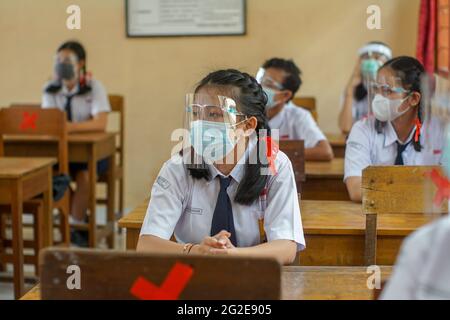 BALI,INDONESIA-MAY 18 2021: Students in Indonesia are following the learning process in class using faceshields and health masks to implement health p Stock Photo