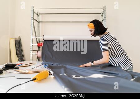 Young tailor take roll of fabric to cur pattern textile measure working on new collection in atelier Stock Photo