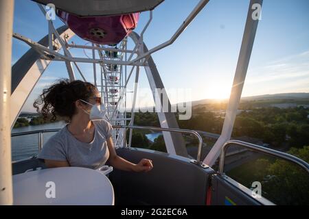 Eltville Am Rhein, Germany. 10th June, 2021. A woman wearing a mouth and nose guard rides a Ferris wheel on the banks of the Rhine in Hesse. Due to the Corona pandemic, many job opportunities for showmen are falling away. As a temporary solution, showmen from Hesse and Rhineland-Palatinate have set up their businesses in Eltville over the summer. (to dpa 'On the situation of showmen in Hesse and Rhineland-Palatinate') Credit: Sebastian Gollnow/dpa/Alamy Live News Stock Photo