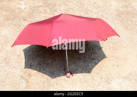 UV umbrella in the summer sun. Red color beach umbrella blocking the sunlight. Shadow on the sandy floor. Sunbath tanning shade shadow background. Stock Photo