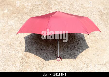 UV umbrella in the summer sun. Red color beach umbrella blocking the sunlight. Shadow on the sandy floor. Sunbath tanning shade shadow background. Stock Photo