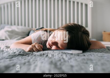 Caucasian school girl 8-9 years read a book and fell asleep. Child tired, lying on bed. Lifestyle Stock Photo