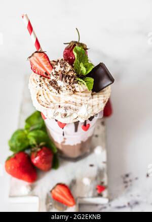 Chocolate and strawberry milkshake with ice cream and whipped cream, mini meringue, chocolate, strawberry and mint served in a glass. Selective focus. Stock Photo