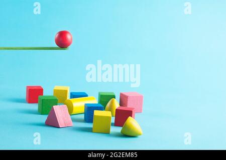 Colorful objects jumping from a green wooden springpoard on blue background. Stock Photo