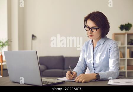 Serious concentrated woman watching video lecture or attending webinar on laptop Stock Photo