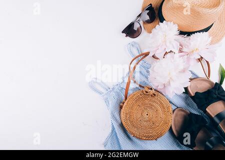 Feminine summer accessories: dress, rattan bag, straw hat, sandals, peony on white background. Stock Photo