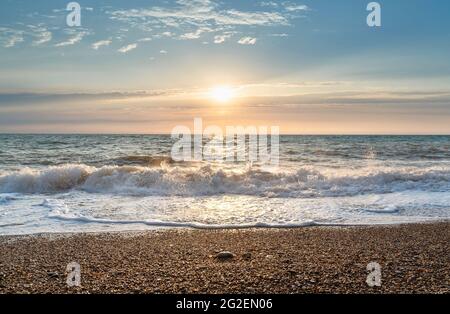 Green blue sea splashing waves backlit by setting sun in front of beautiful sunset sky background. Travel and tourism concept. Nature background. Grea Stock Photo