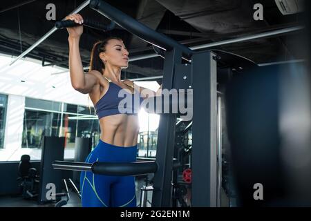 Athletic girl doing exercises on assisted pull-up machines at gym Stock Photo