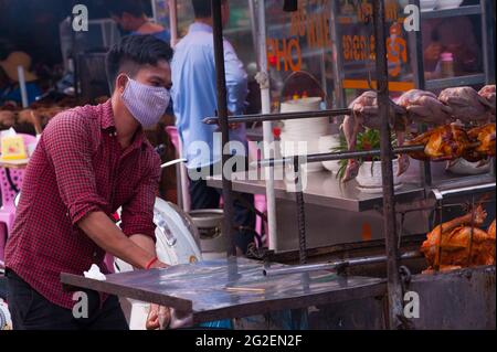 A Cambodian man, wearing a protective face mask / covering, sells grilled chicken at Kandal Market during the coronavirus pandemic. Phnom Penh, Cambodia. March 25th, 2020. © Kraig Lieb Stock Photo