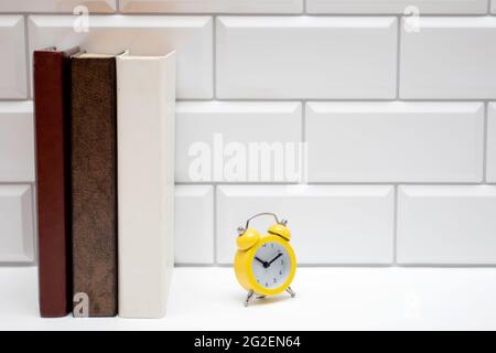 BookShelf with blank books and yellow alarm clock on white brick wall Stock Photo