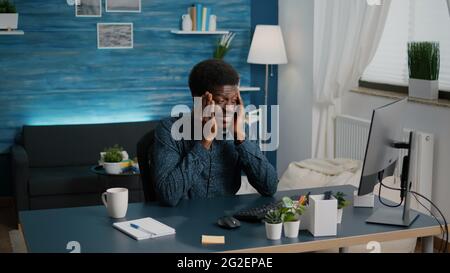 African american guy stressing, having a big headache while rubbing his temples in cozy flat, overworked exhausted suffering black man. Tired overwhelmed person from to much work Stock Photo