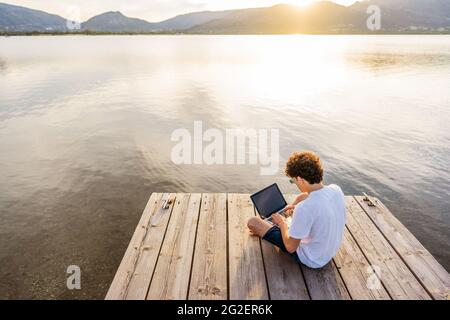 Nerd guy spending time outdoor programming at sunset writing code using laptop. New job opportunity at modern times to work everywhere using notebook Stock Photo