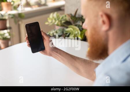Man holding a black mobile phone with blank screen, using new mobile app, male hand with smartphone, back view, copy space for advertising, promotion Stock Photo