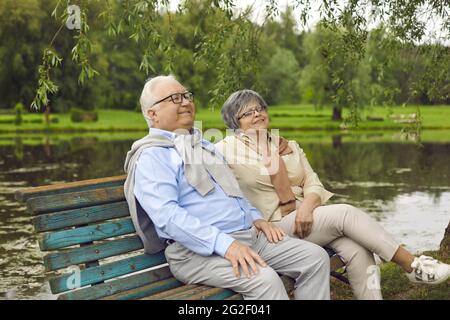 Happy senior couple sitting on an old wooden bench under a tree in a summer park Stock Photo