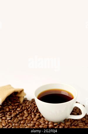 Cup of hot coffee with roasted coffee beans scattered from burlap bag on white background Stock Photo