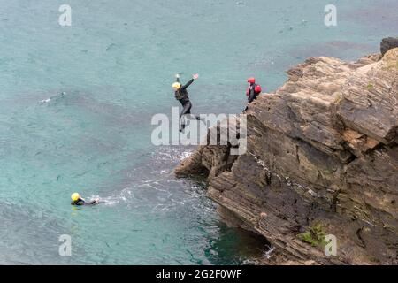 A holidaymaker leaping from rocks during a coasteering session around the inter tidal zone at Towan head in Newquay in Cornwall. Stock Photo