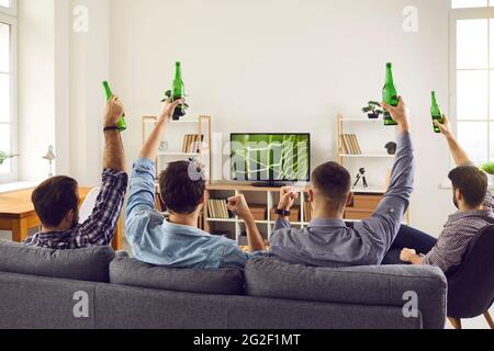 A group of young friends are watching a home soccer game on TV, holding a bottle Stock Photo