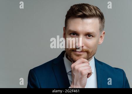 Handsome thoughtful entrepreneur thinking about business and looking at camera while standing against grey background Stock Photo