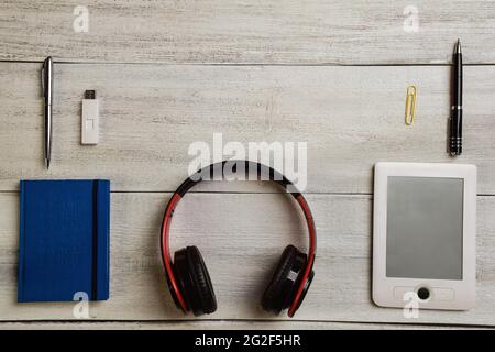 An e-book, two pens, a notebook, wireless headphones and a flash drive are on a light wooden table Stock Photo