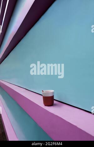 Colored pink and turquoise wall going into perspective. There is a pink cup of coffee on the curb Stock Photo