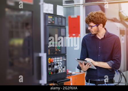 Young American engineer worker working programing heavy industrial machine in factory. employee looking and control CNC machine in production line. Stock Photo