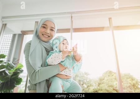 Muslim Hijab holding support her child baby happy smiling at home. mother care healthy infant looking camera. Stock Photo