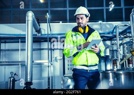 Factory worker engineer working in factory using tablet computer to check maintenance boiler water pipe in factory. Stock Photo