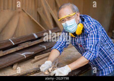 Portrait of elder wood worker hobby for good retirement, Asian male mature professional master of wood craft furniture wooden maker man. Stock Photo