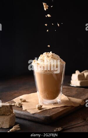 Sprinkles halawa in trendy recipe coffee latte with halva in modern glass cup on dark brown background. Vertical. Close up. Stock Photo