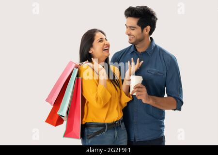 A YOUNG MAN HAPPILY LOOKS AT WIFE WHILE SHE LAUGHS HOLDING SHOPPING BAGS IN HAND Stock Photo